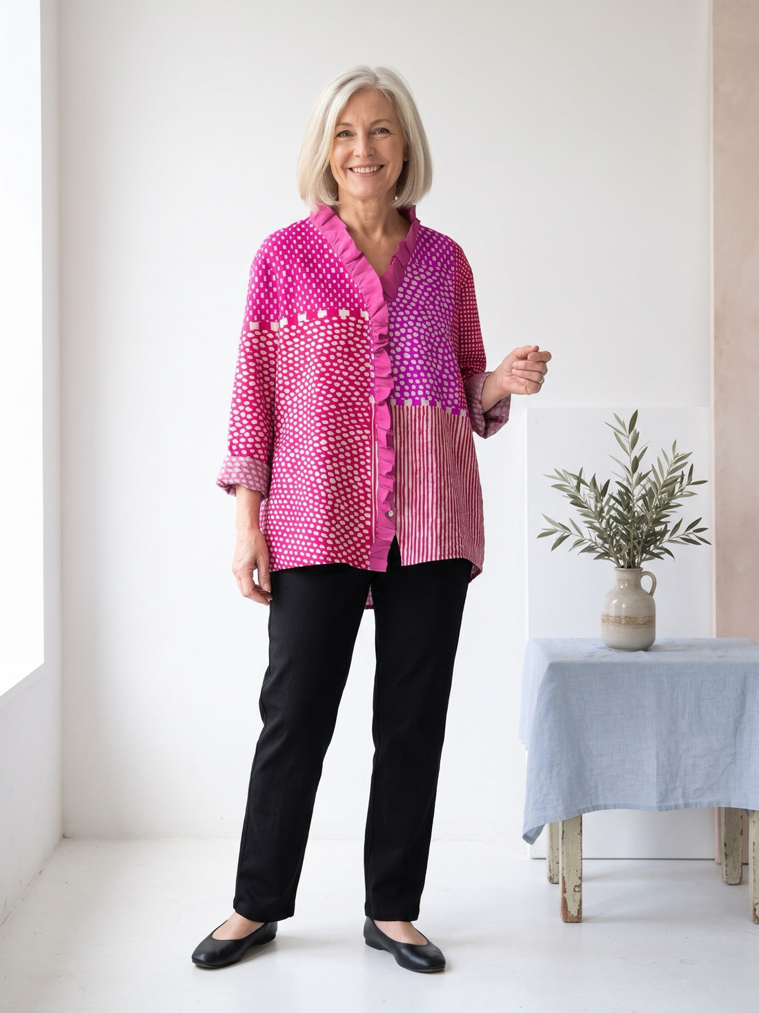 Woman in her late fifties wearing the Pink Polka Dot Patchwork Shirt with black trousers