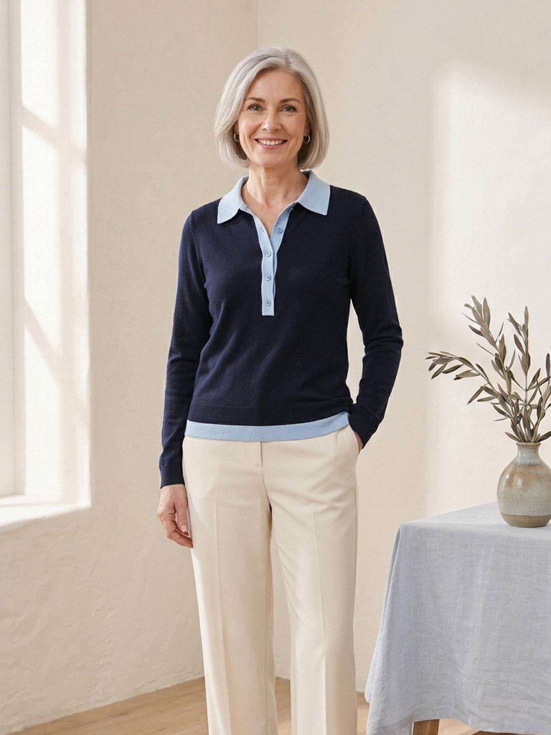 Woman in her fifties wearing the navy Polo-Collar Layered Jumper with cream trousers