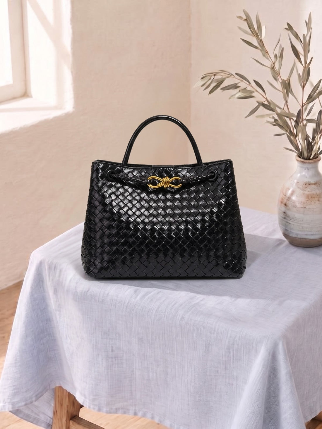 Woven Top-Handle Bag in Black on a linen-covered stool